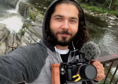 Filmmaker Hasi Eldib takes a smiling selfie while standing above the river